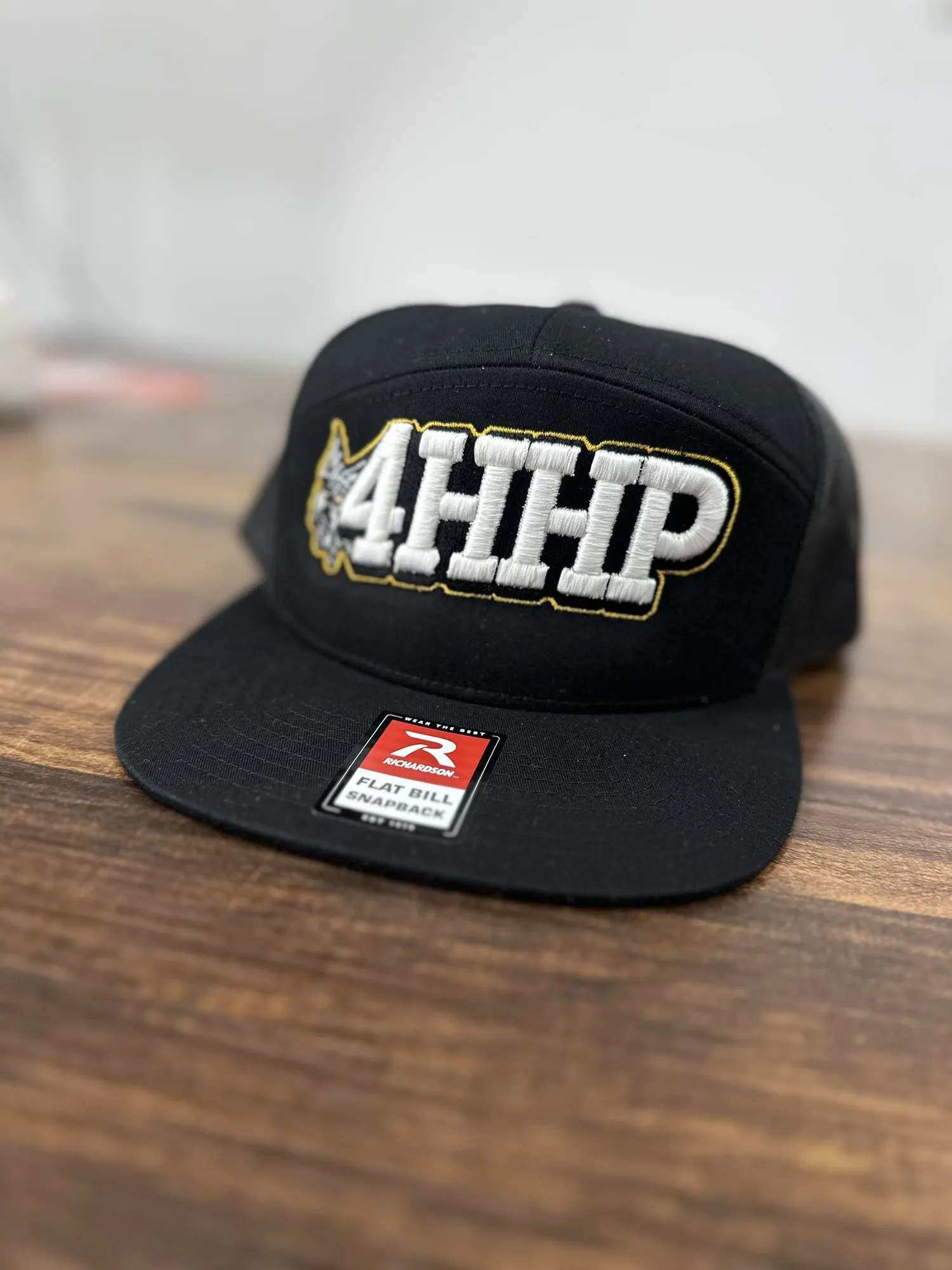 Black flat bill snapback with a raised white 4HHP logo outlined in gold
