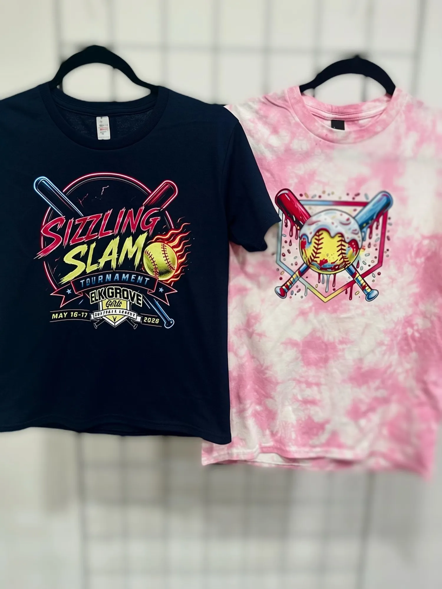 Two youth softball tournament shirts, a navy Sizzling Slam design and a pink tie-dye softball design