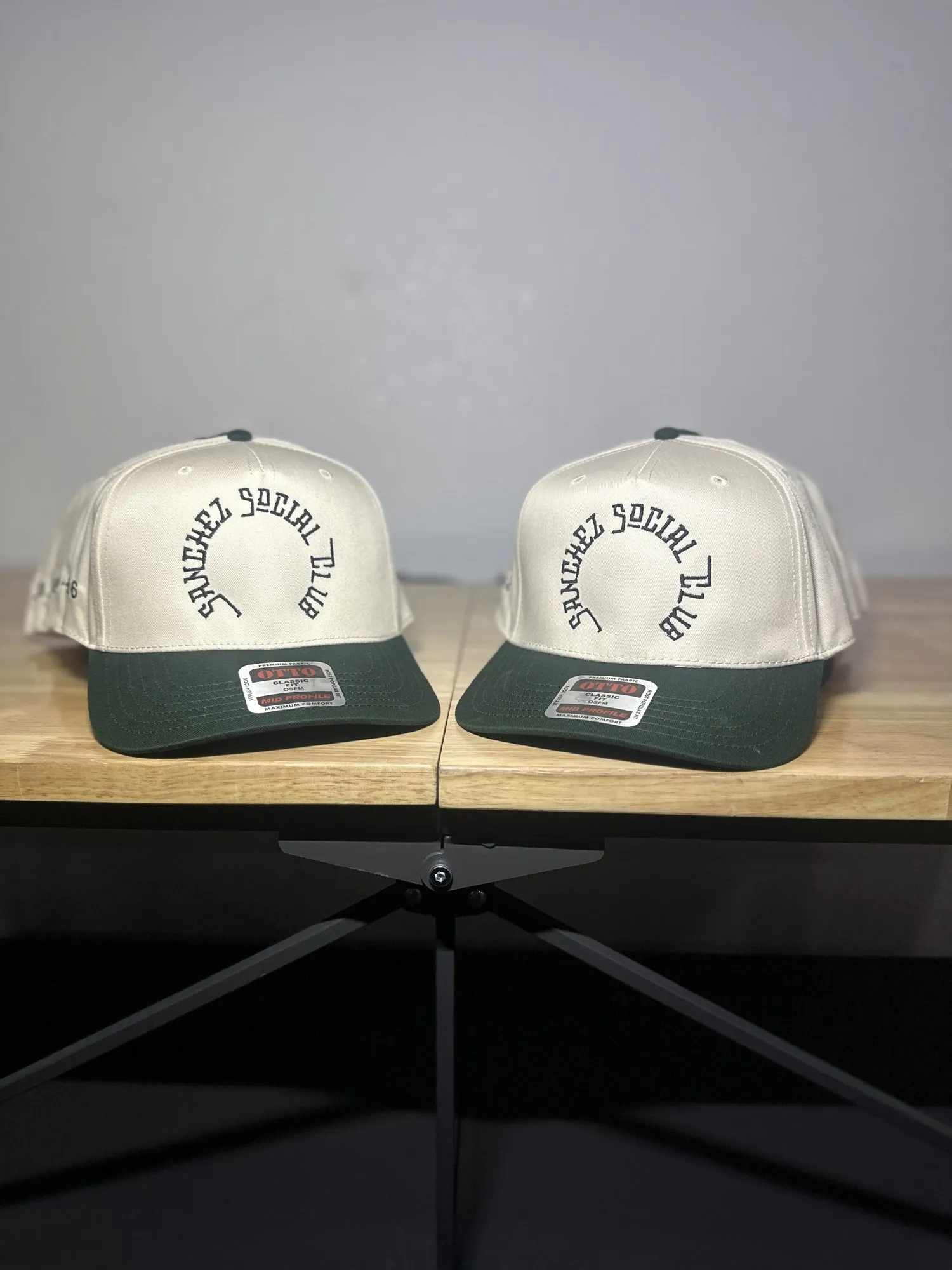 Two cream and green snapback hats embroidered with Sanchez Social Club in black script
