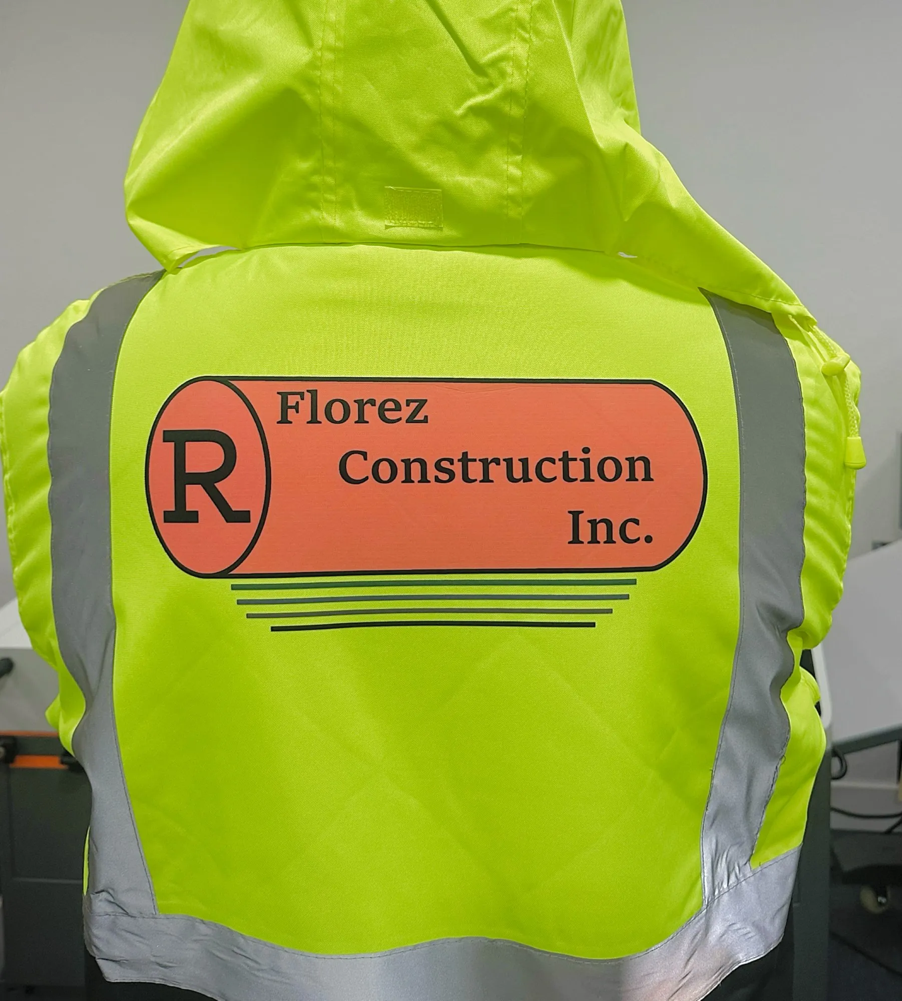 Back of a hi-vis yellow jacket printed with the R Florez Construction Inc. logo