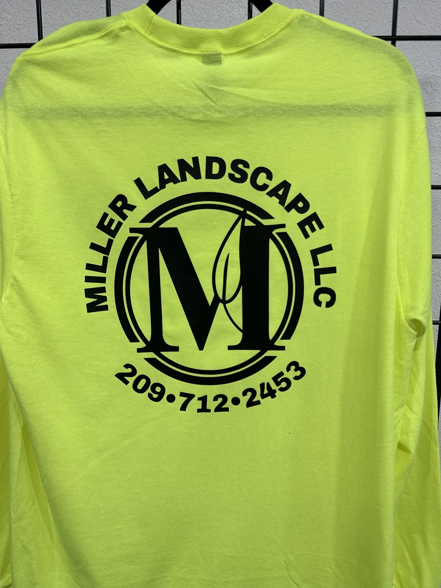 Back of a safety yellow long sleeve shirt printed with the Miller Landscape LLC logo and phone number