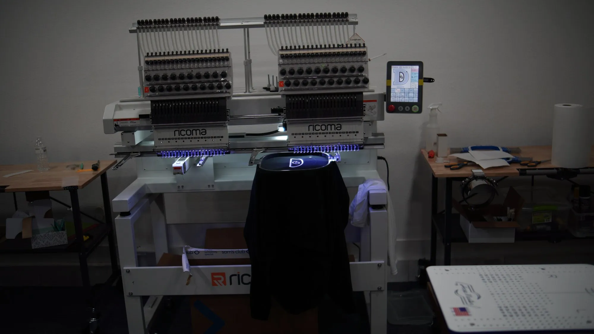 Two-head commercial embroidery machine stitching a logo onto a black shirt in the 4 His Highest Promotions shop