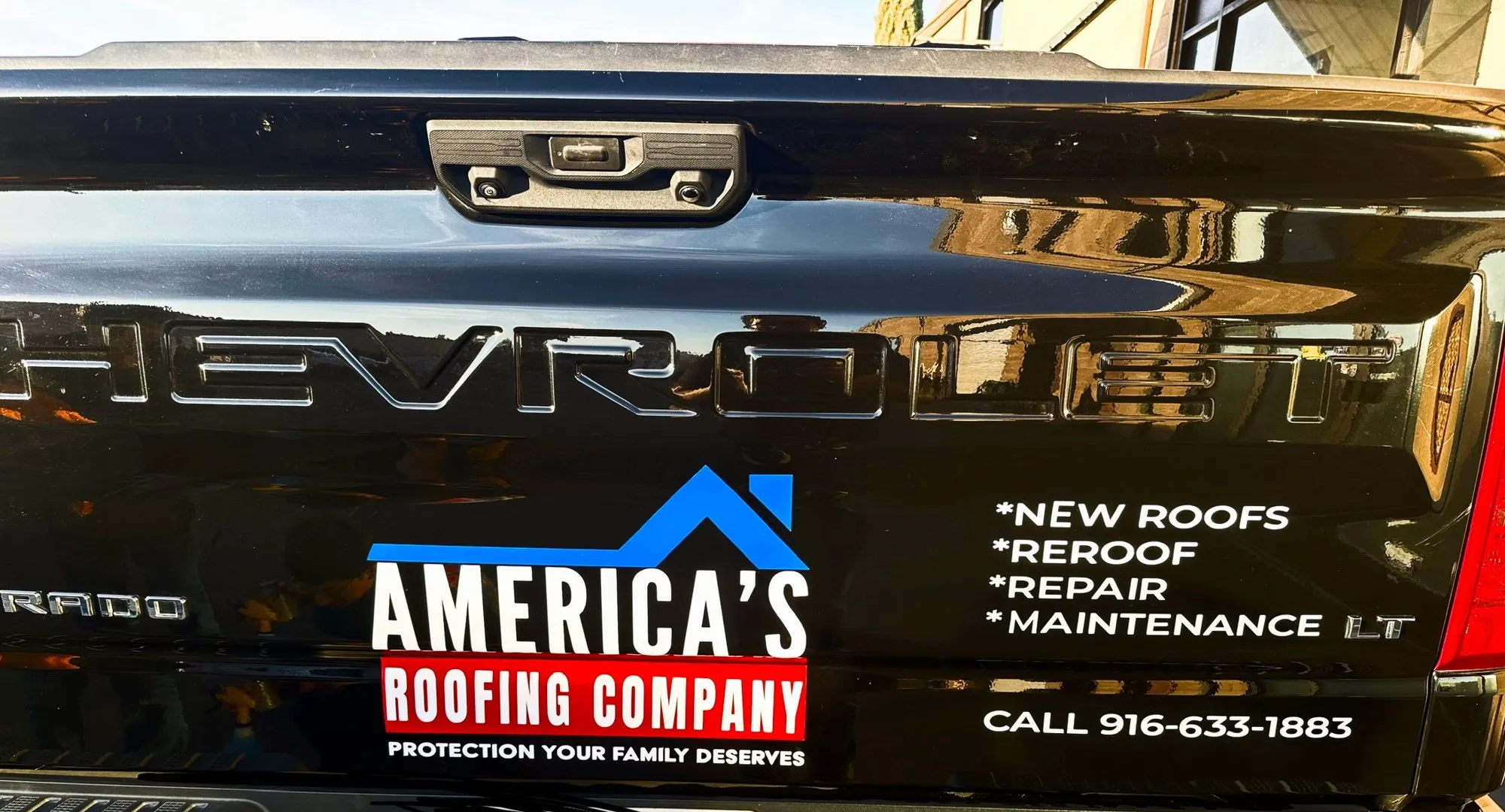 Vinyl decal on a black truck tailgate for America's Roofing Company, listing new roofs, reroofs, repair and maintenance