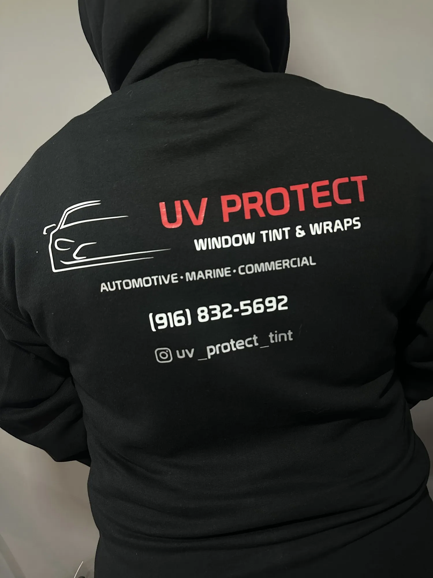 Back of a black hoodie printed with the UV Protect Window Tint and Wraps logo in red and white